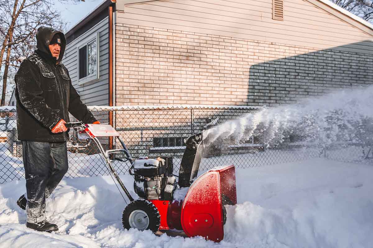 Man uses snow blower in the backyard