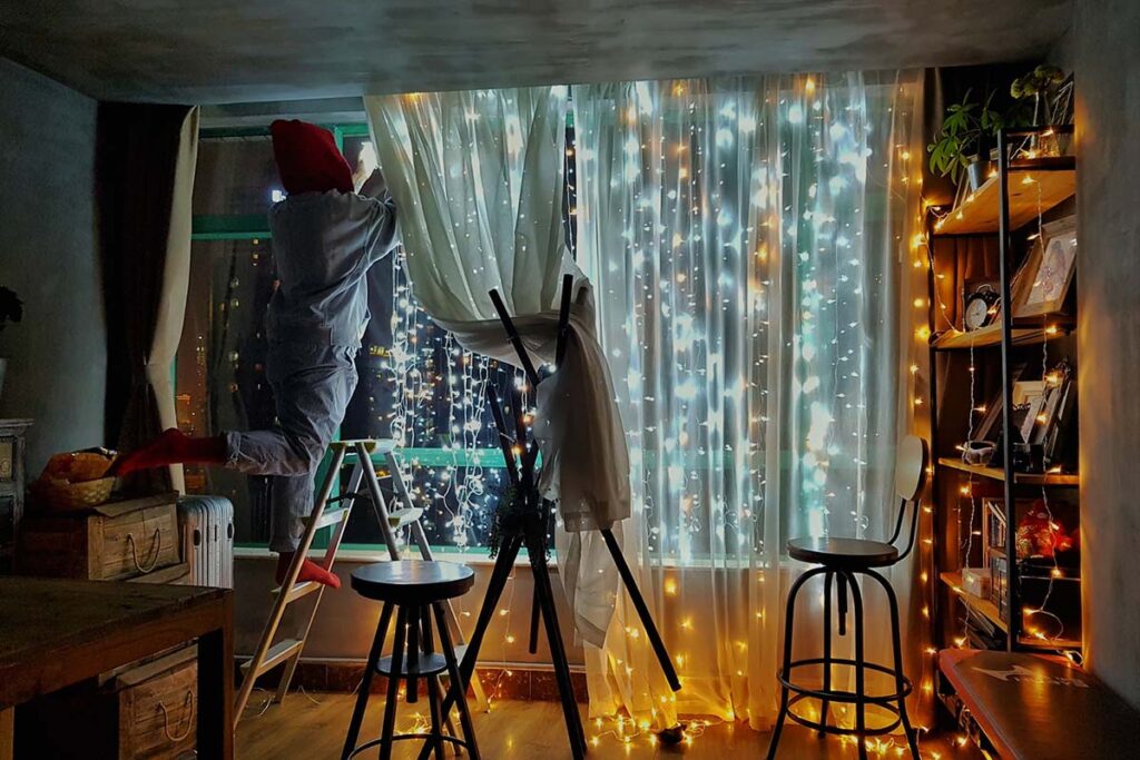 people hanging curtain lights in living room