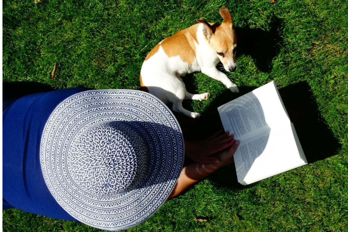 A woman lying on the grass with her dog and reading a book in a pet-friendly garden.